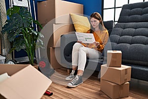 Young brunette woman sitting on the sofa at new home looking at documents thinking attitude and sober expression looking self