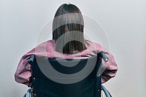 Young brunette woman sitting on wheelchair standing backwards looking away with arms on body