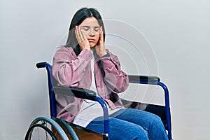 Young brunette woman sitting on wheelchair tired hands covering face, depression and sadness, upset and irritated for problem