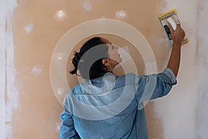 Young brunette woman smooths a plastering indoor wall