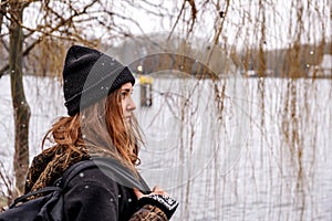 Young brunette woman standiing by a lake on snowy day looking pensive