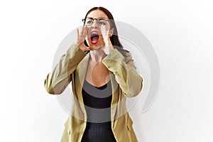 Young brunette woman standing over isolated background shouting angry out loud with hands over mouth