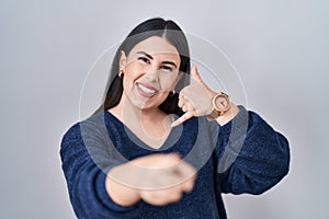 Young brunette woman standing over isolated background smiling doing talking on the telephone gesture and pointing to you