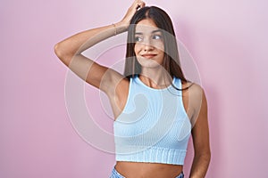 Young brunette woman standing over pink background confuse and wondering about question