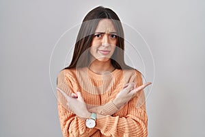 Young brunette woman standing over white background pointing to both sides with fingers, different direction disagree