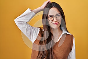 Young brunette woman standing over yellow background wearing glasses confuse and wonder about question