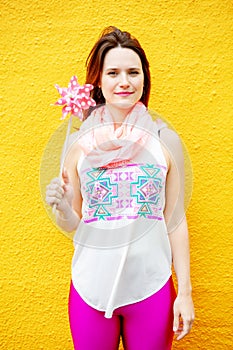 Young woman standing at yellow wall with pinwheel