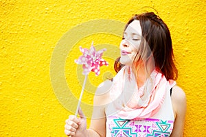 Young woman standing at yellow wall with pinwheel