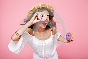 Young brunette woman in straw hat, holding fresh donut as teles