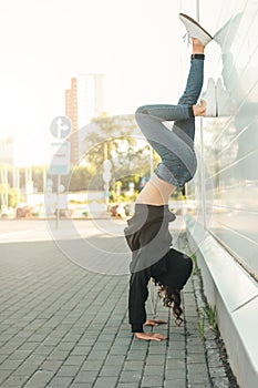 Young brunette woman street dancer gymnast standing on her arms on city