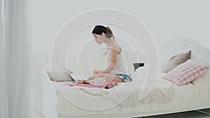 Young brunette woman stretches on a bed. Beautiful girl using laptop during breakfast. Drinking juice and dancing.