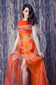 Young brunette woman in stylish orange silk dress posing on wood