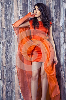 Young brunette woman in stylish orange silk dress posing on wood