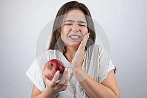 Young brunette woman suffering toothache holding red apple in her hand standing on isolated white background healthcare