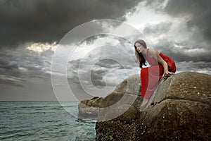Young brunette woman in summer red dress sits on stone