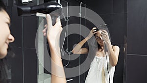 Young brunette woman in towel drying hair with hairdryer in bathroom