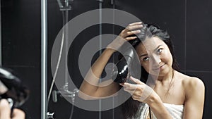 Young brunette woman in towel drying hair with hairdryer in bathroom