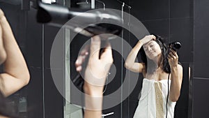 Young brunette woman in towel drying hair with hairdryer in bathroom