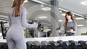 A young brunette woman trains her biceps by lifting a dumbbell. Training in the gym