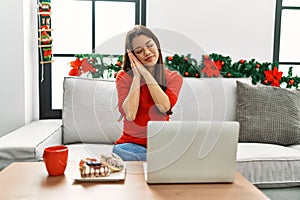 Young brunette woman using laptop sitting on the sofa on christmas sleeping tired dreaming and posing with hands together while