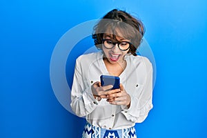 Young brunette woman using smartphone celebrating crazy and amazed for success with open eyes screaming excited