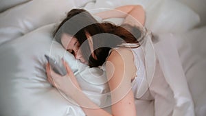 Young brunette woman wakes up from an alarm clock on a mobile phone, turns off the alarm and sleeps on.