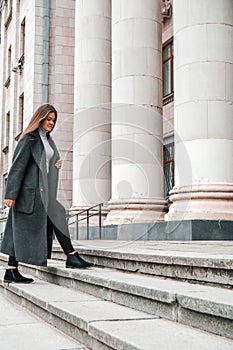 Young brunette woman walking up on stairs. Long beautiful hair and long coat in business downtown. Careerist. Women