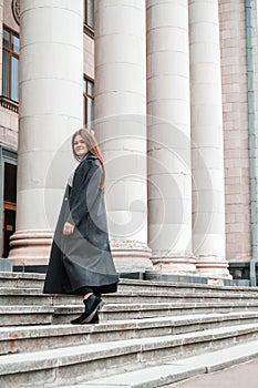 Young brunette woman walking up on stairs. Long beautiful hair and long coat in business downtown. Careerist. Women