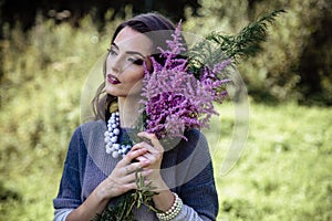 Young brunette woman walks in a summer forest park wearing stylish casual clothes