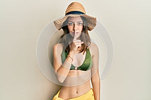 Young brunette woman wearing bikini asking to be quiet with finger on lips