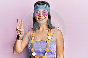 Young brunette woman wearing bohemian and hippie style smiling with happy face winking at the camera doing victory sign