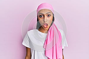 Young brunette woman wearing breast cancer support pink scarf scared and amazed with open mouth for surprise, disbelief face