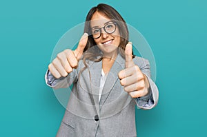 Young brunette woman wearing business clothes approving doing positive gesture with hand, thumbs up smiling and happy for success