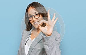 Young brunette woman wearing business clothes smiling positive doing ok sign with hand and fingers