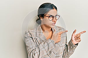 Young brunette woman wearing business jacket and glasses pointing aside worried and nervous with both hands, concerned and