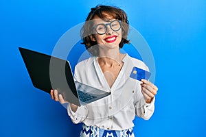 Young brunette woman wearing business style holding laptop and credit card smiling with a happy and cool smile on face