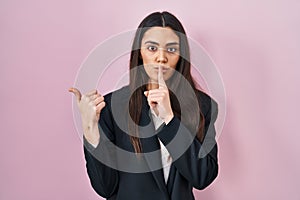 Young brunette woman wearing business style over pink background asking to be quiet with finger on lips pointing with hand to the