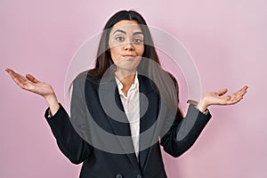 Young brunette woman wearing business style over pink background clueless and confused expression with arms and hands raised