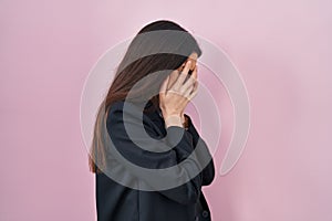 Young brunette woman wearing business style over pink background with sad expression covering face with hands while crying