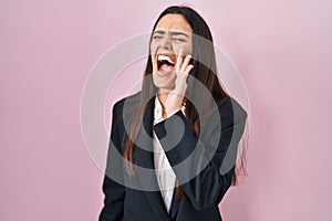 Young brunette woman wearing business style over pink background shouting and screaming loud to side with hand on mouth