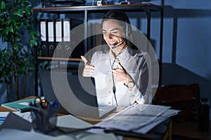 Young brunette woman wearing call center agent headset working late at night approving doing positive gesture with hand, thumbs up