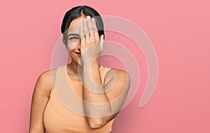 Young brunette woman wearing casual clothes covering one eye with hand, confident smile on face and surprise emotion