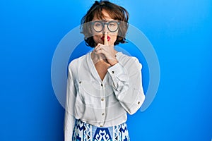Young brunette woman wearing casual clothes and glasses asking to be quiet with finger on lips