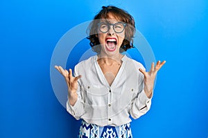 Young brunette woman wearing casual clothes and glasses crazy and mad shouting and yelling with aggressive expression and arms