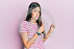 Young brunette woman wearing casual clothes over pink background pointing aside worried and nervous with both hands, concerned and