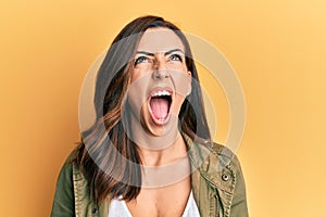 Young brunette woman wearing casual clothes over yellow background angry and mad screaming frustrated and furious, shouting with