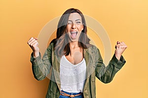 Young brunette woman wearing casual clothes over yellow background screaming proud, celebrating victory and success very excited