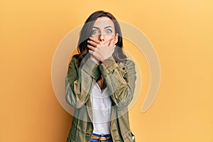 Young brunette woman wearing casual clothes over yellow background shocked covering mouth with hands for mistake