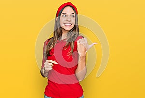 Young brunette woman wearing casual clothes smiling with happy face looking and pointing to the side with thumb up