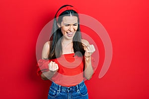 Young brunette woman wearing casual red shirt celebrating surprised and amazed for success with arms raised and eyes closed